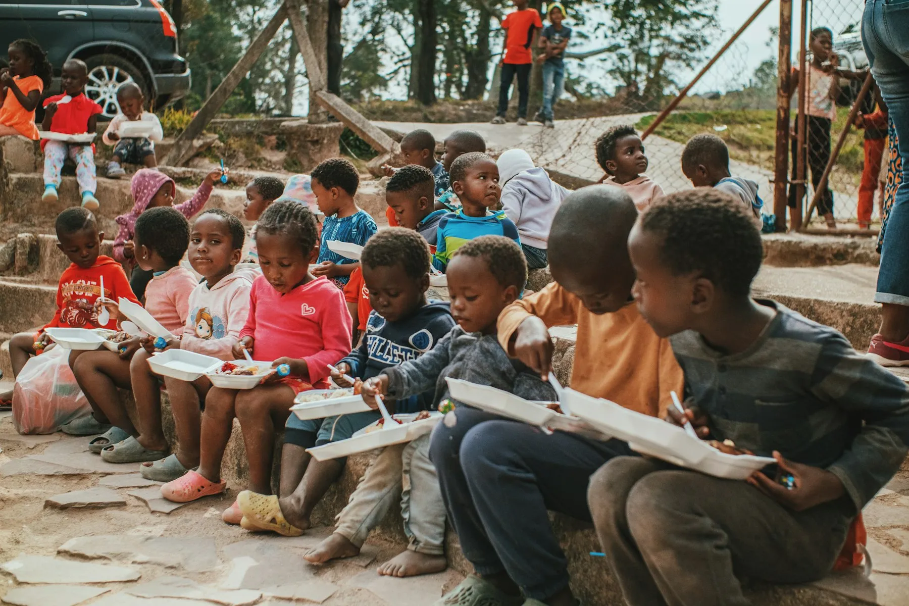 Children sitting on outdoor steps, reading and writing in their books