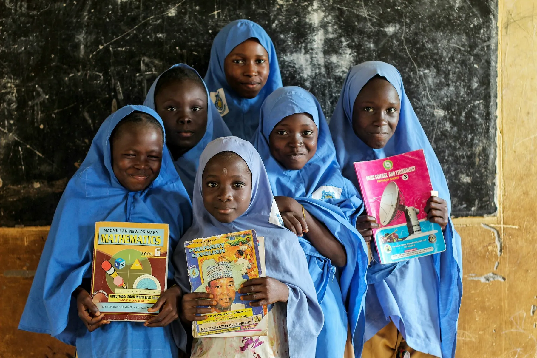 Schoolgirls in blue hijabs smiling and holding up their books